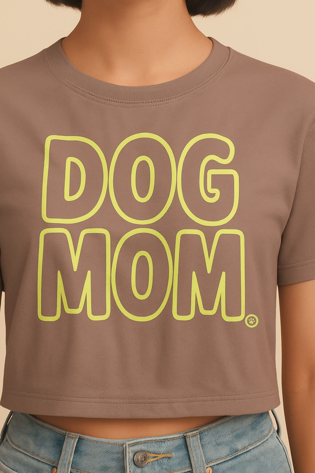 A person models an Oversized Dog Mom Crop Top from Dogloverclothing.com in brown with bold yellow-green DOG MOM text, paired with light blue jeans. The cropped image focuses on the Dog Mom lifestyle.