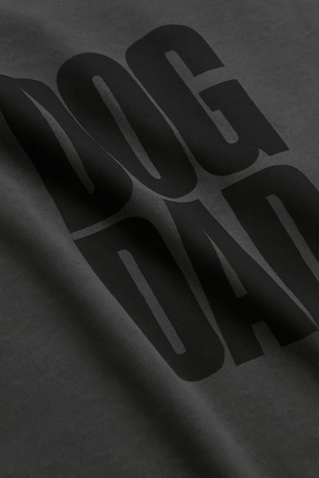 Close-up of the Oversized Dog Dad T-Shirt by Dogloverclothing.com, featuring bold black DOG DAD text in large, overlapping letters on durable dark cotton fabric in a relaxed fit.
