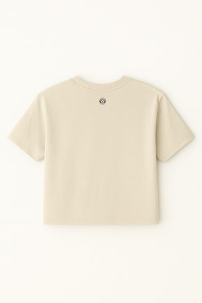 The Oversized Dog Mom Crop Top by Dogloverclothing.com is a relaxed fit beige crop top, shown from the back with a small round emblem at the neckline—ideal for embracing a casual Dog Mom Lifestyle.