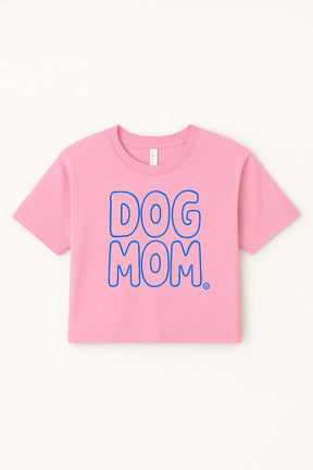 The Oversized Dog Mom Crop Top by Dogloverclothing.com is a pink, relaxed fit crop top in soft combed cotton with DOG MOM. in bold blue-outlined letters on the front, shown laid flat on a light background.