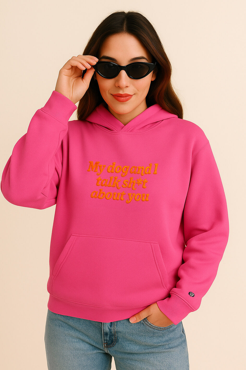 A woman with long brown hair wears black sunglasses and blue jeans, styled in the Bold My Dog And I Talk Embroidered Hoodie from Dogloverclothing.com against a beige background. The bright pink hoodie features yellow text on premium fabric.