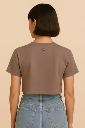 A person with short brown hair is shown from the back wearing the Oversized Dog Mom Crop Top by Dogloverclothing.com and high-waisted light blue jeans against a beige background, capturing an effortless Dog Mom Lifestyle vibe.