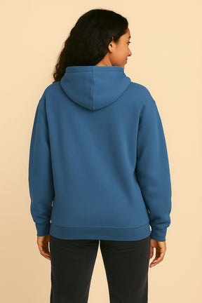 A person with long, dark, wavy hair is shown from the back, wearing the ultra-soft Dog Mom Hoodie by Dogloverclothing.com and black pants, standing against a plain beige background.