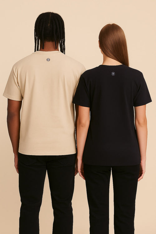 Two people stand back-to-back against a beige background wearing black pants. One wears the Relaxed Dog Walker© Unisex T-Shirt by Dogloverclothing.com in beige with braided hair; the other wears the same shirt in black with straight light brown hair.