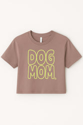 The Oversized Dog Mom Crop Top by Dogloverclothing.com features bold yellow DOG MOM bubble letters on brown fabric, styled in a relaxed fit—perfect for showing off your dog mom lifestyle. Displayed against a plain light background.
