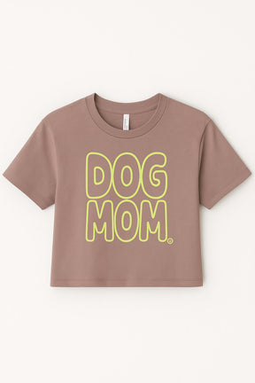 The Oversized Dog Mom Crop Top by Dogloverclothing.com features bold yellow DOG MOM bubble letters on brown fabric, styled in a relaxed fit—perfect for showing off your dog mom lifestyle. Displayed against a plain light background.