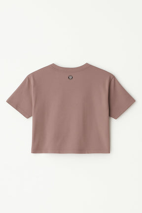 An Oversized Dog Mom Crop Top from Dogloverclothing.com, taupe and short-sleeved, is laid flat with the back facing up, featuring a small round logo near the upper center neckline.