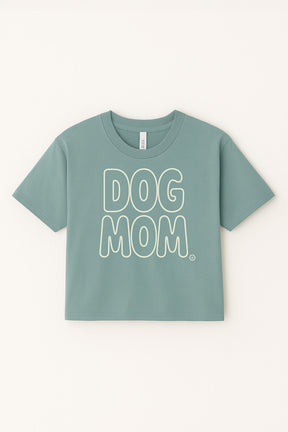 The Oversized Dog Mom Crop Top from Dogloverclothing.com is light green, made of 100% combed cotton, with a relaxed fit and bold white DOG MOM lettering on the front.